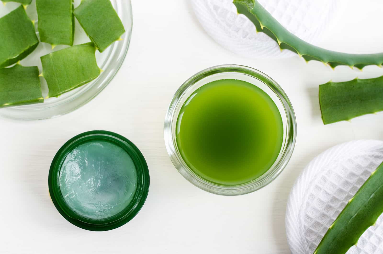 Small glass bowl with aloe vera juice and jar of aloe vera healing balm. Homemade facial toner or hair mask (moisturizer). Natural beauty treaments and spa. White background. Top view, copy space. Small glass bowl with aloe vera juice and jar of aloe vera healing balm. Homemade facial toner or hair mask (moisturizer). Natural beauty treaments and spa. White background. Top view, copy space.